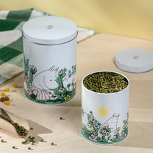 Load image into Gallery viewer, Two white tins with illustrations of Moomin characters, Moominmamma and Moomin in the garden with a full sun in the sky. One of the tins is open and is filled with lentils.