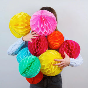 A woman is seen holding a whole bunch of honeycomb ball decorations in different colours