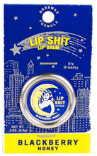 Load image into Gallery viewer, A silver tin of 'lip shit' lip balm with a picture of a moon embracing a woman. Tin is backed on a navy blue card with a simple outline of a starry city skyline. Fonts are contrasting navy and bright yellow.