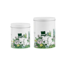 Load image into Gallery viewer, Two white cylindrical tins with Moominpappa and Little My, Moomin characters, relaxing amongst the green grass and yellow and pink flowers on a white background