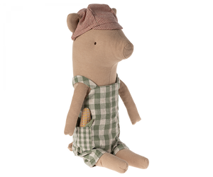 Soft toy pig wearing a striped red and cream cap with his ears sticking out through slits, and wearing green and white gingham overalls.  He has a toy baguette sticking out of his pocket