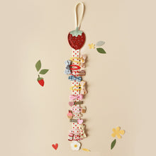 Load image into Gallery viewer, This hair clip hanger has a ribbon hanging hook at the top, below which is a glittery fabric strawberry.  Attached is a length of soft white ribbon with little red dots which is the perfect size for clipping on hair clips for neat and accessible storage.  At the bottom of the ribbon length there is a little felt daisy.  The clip hanger is shown here with 12 different hair clips on it.