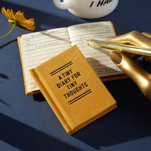 Load image into Gallery viewer, the tiny mustard coloured diary can be seen with its cover with the words in black capitals saying &#39;A TINY DIARY FOR THOUGHTS&#39;.  Underneathe the closed diary is an open one revelaing the inside sheets which are lined with a place for the date and to number the topic and &#39;brilliant realization&#39;
