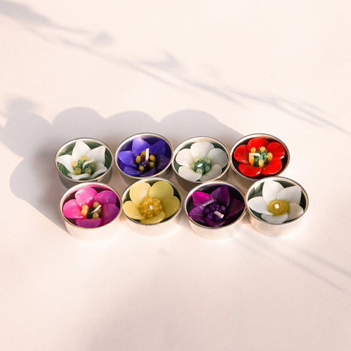 8 tea lights, each one is delicately modelled to look like a different flower. Colours used include purple, yellow, red and pink.