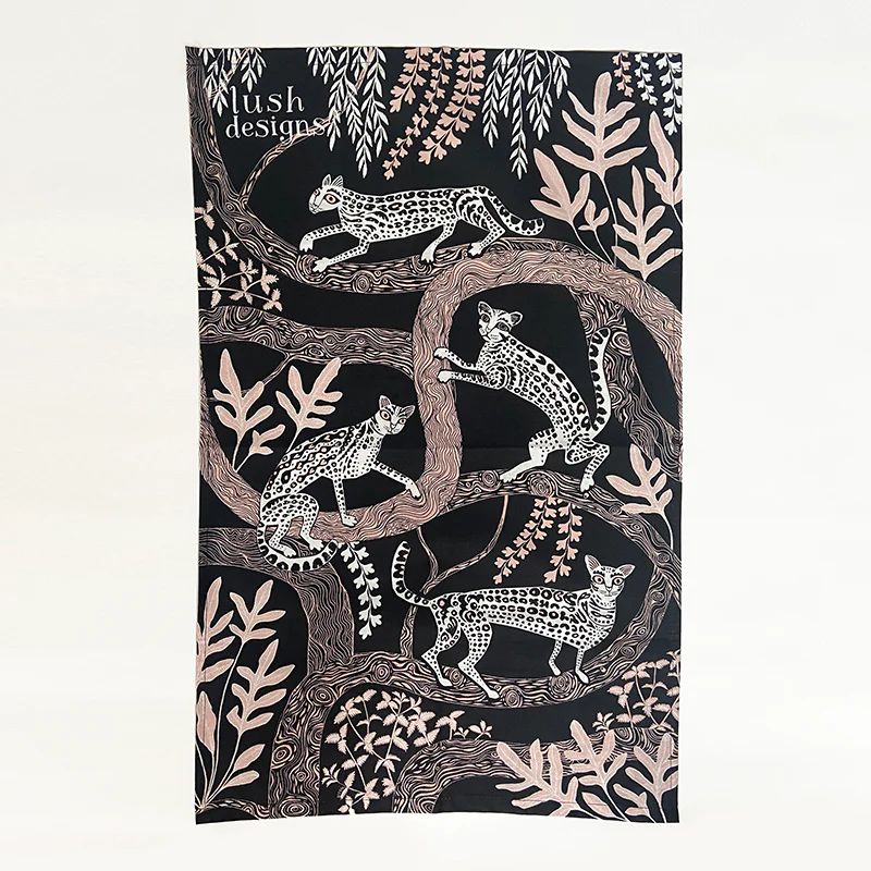 this teatowel has a black background and features an all over design with tree branches and foliage on which four beautiful ocelots are climbing.