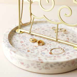 Sunshine Jewellery Stand by Lisa Angel | £22.00. The arched frame is made of gold metal and features a beaming sun design complete with cloud detailing. On the round sun face are holes for studs and hook earrings, while the edge of the frame has pegs made for your necklaces and longer pieces. The base of this stand is made of terrazzo resin in speckled whites, creams and greys to finish this sweet jewellery storage piece. 