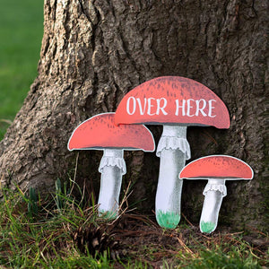 Some more picture props: 3 red capped mushrooms, one of which says "over here" can be seen propped up against a tree.