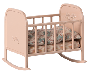 A light pink metal cradle with stripey matress and floral duvet and pillow in muted colours