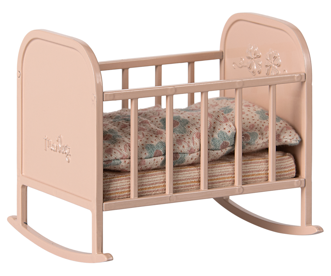 A light pink metal cradle with stripey matress and floral duvet and pillow in muted colours