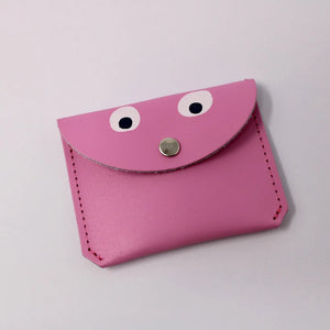 bright pink leather mini purse. Simple design with stitching up the sides. it has a front flap with a small silver popper, which also looks like a nose as there are 2 simple white and black googly eyes painted on to the leather, making the purse have a little face.