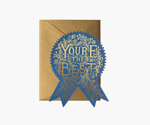 Die cut card in the shape of a rosette, with a dark blue background.  Goid lettering reads You’re The Best, around the words is a beautiful floral design also in gold foil. Its gold enevelope isnlying under the card.