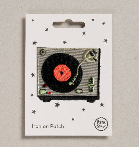 The iron on patch is pictured on its backing card with little stars on.  The patch depicts a turntable from above, with a record playing.