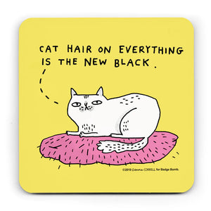 A yellow square coaster with an illustration by Gemma Correll of a white cat sitting on a pink cushion.   A dotted line form the cat's head goes to the words above "Cat hair on everything is the new black".  The cushions has lots of little hairs all over it.