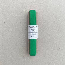 Load image into Gallery viewer, A 5-meter roll of bright green cotton ribbon with a white paper label, placed on a textured gray surface.
