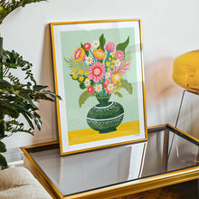 Load image into Gallery viewer, Framed artwork of a colorful floral bouquet on a table with a plant and lamp in the background.
