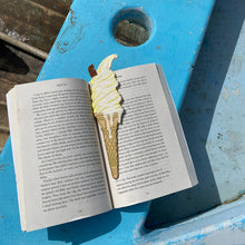 Load image into Gallery viewer, Embroidered ice cream bookmark inside a paper book on the beach.
