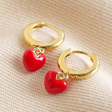 Load image into Gallery viewer, small gold huggie hoops with bright red little heart charms hangiong from them
