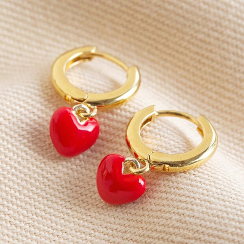 small gold huggie hoops with bright red little heart charms hangiong from them