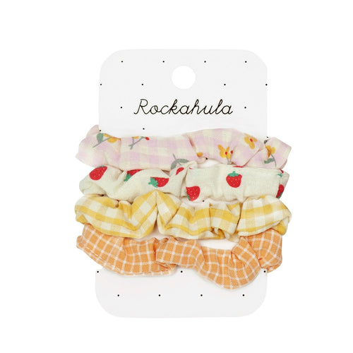 Pack of 4 scrunchies seen here on their merchandising card with rockahula at the top.  The first is pink gingham with flowers.  The second is soft white with small strawberries, the third is yellow gingham and the fourth is orange with a white check.