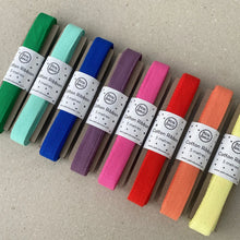 Load image into Gallery viewer, Eight rolls of cotton ribbon in assorted colors, including green, mint, light blue, royal blue, purple, pink, red, orange, and pale yellow, arranged diagonally on a light gray textured surface. Each roll has a white paper band labeled 'Cotton Ribbon 5 metres'.
