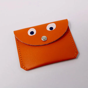 bright orange leather mini purse.  Simple design with stitching up the sides.  It has a front flap with a small silver popper, which also looks like a nose as there are 2 simple white and black googly eyes painted on to the leather, making the purse have a little face.