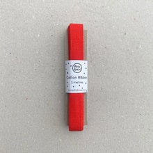 Load image into Gallery viewer, A 5-meter roll of red cotton ribbon, wrapped in a white paper band, set against a neutral gray textured background.
