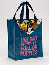 Load image into Gallery viewer, Cute little tote bag by blue Q featuring an illustration by John Bond. The bag is mostly dark petrol blue with bright pink lettering which reads “THIS BAG MIGHT BE FULL OF PUPPIES”. At the top edge of the bag 9 little assorted puppies can be seen, as if they are pulling the rim of the bag down and are inside.
