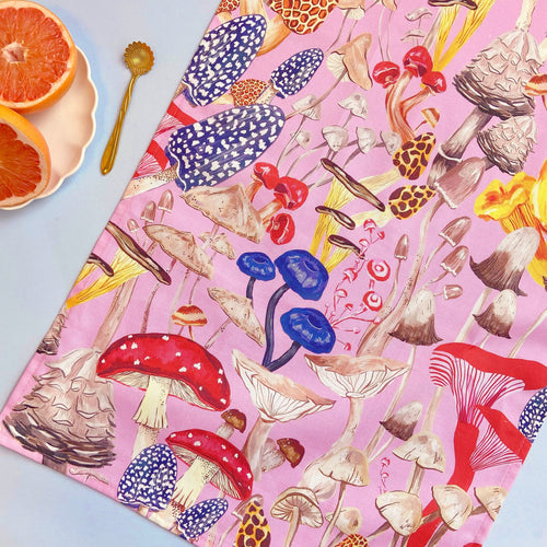 Pink tea towel with a variety of different mushrooms in reds,pinks and blue 
