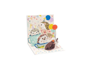 A pop up card with 5 hedgehogs with party hats and balloons in tea cups
