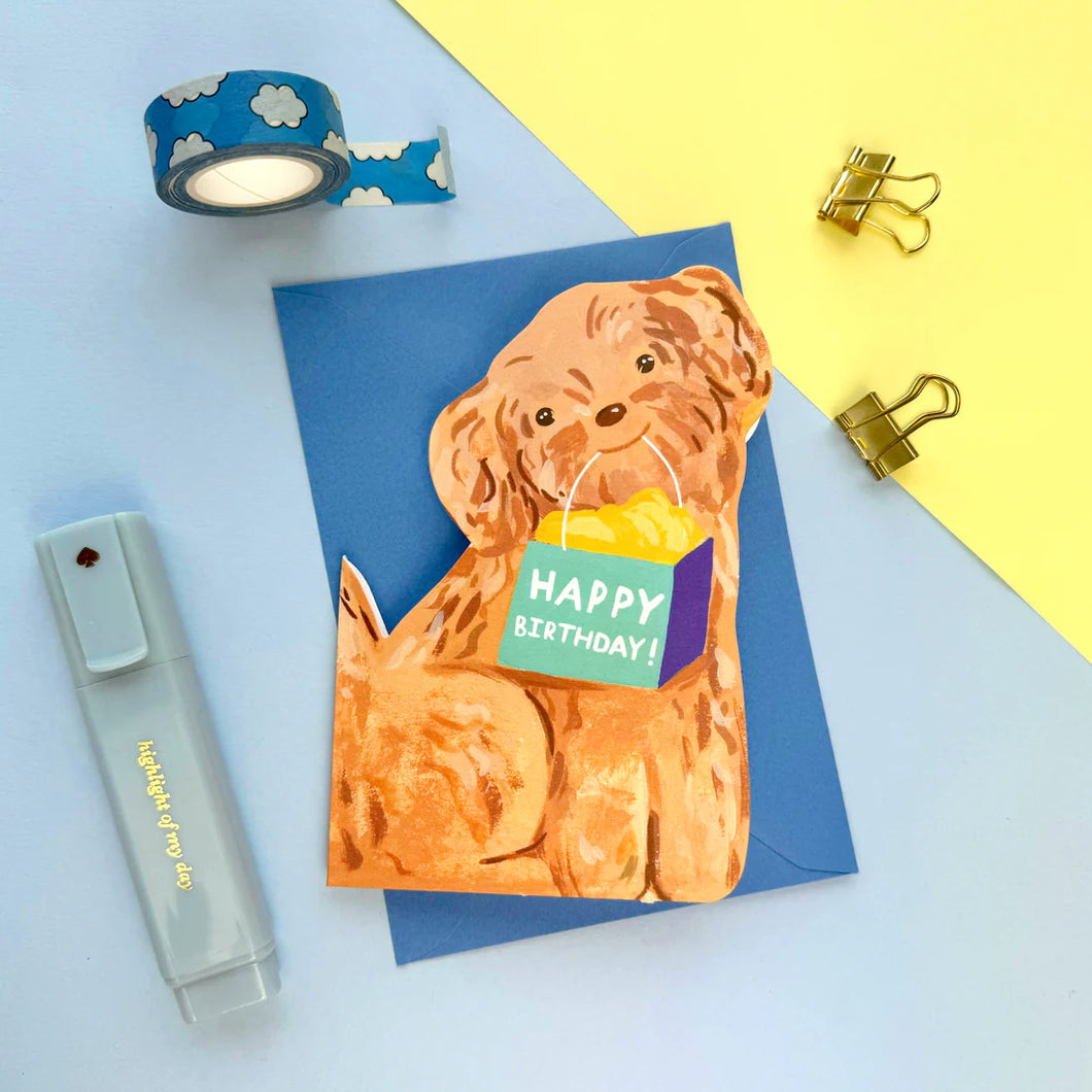 Cut out shaped card featuring a golden coloured happy looking sitting dog with a gift bag in its mouth with the words HAPPY BIRTHDAY! on it