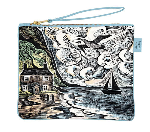 poch bag, with a wrist strap featuring a print by angela harding.  Is is a beach scen with a house and a steep cliff.  There is saling boat on the sea and a bird flying in the sky.  Two figures can be seen on the beach.