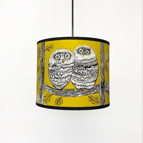 hanging lampshaed with mustard background and a design in black and white featuring baby owls on branches.  There is a black trim to the top and bottom of the shade.