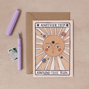 The words 'Another trip around the sun'  surrounding illustration of shining sun with delicate facial features