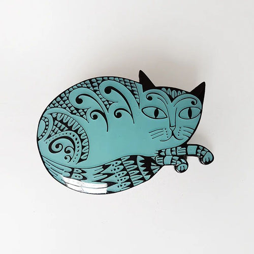 Blue enamel pin badge in the shape of a cat, ilustrated with black swirly designs. The badge is fastened to a light green card