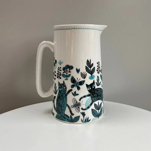 white jug with black and blue design of  cats jumoing around amongst plants and flowers, with insects flying around