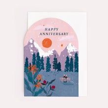 Load image into Gallery viewer, An arc shaped greetings card featuring the words Happy Anniversary with a painted scene of a couple on a bench looking at the sunset over the snowy mountains and trees. Flowers are in the foreground.
