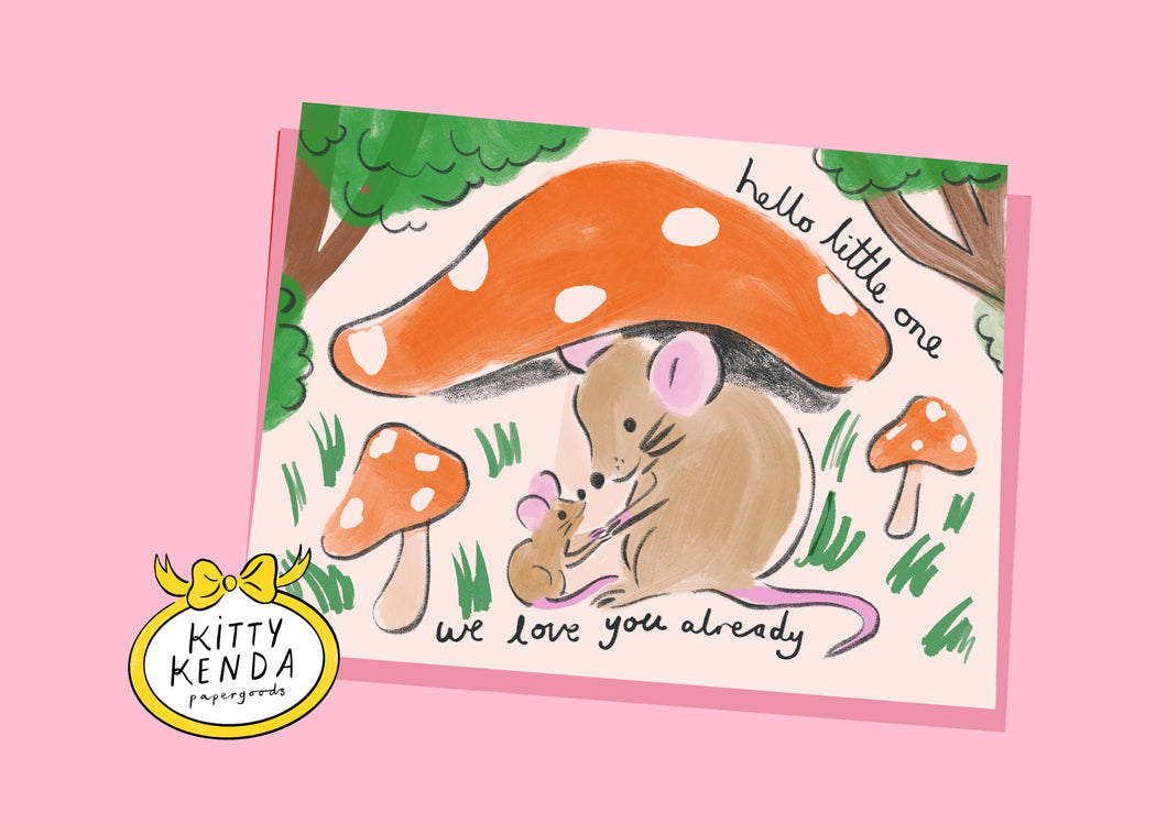 mouse and baby mouse under a red spotty mushroom with other mushrooms and grass around them and trees in the backgound.  The words Hello little one.  We love you already