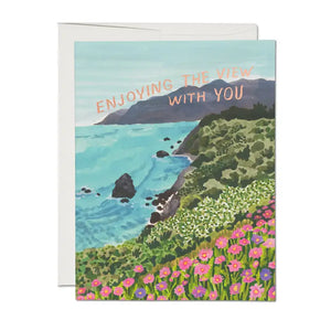 Beautifullu illustrated card featuring a coastal vie with flowers in foreground.  Illustrated by Danielle Knoll.  Red Cap Cards USA.  Reads "enjoying the view with you" in gold lettering.  Suitable for many occasions including valentine's.
