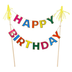 the cake bunting is photographed against a  white background.  The pllain wooden sticks on either side are topeed with yellow paper tassels.  The bunting hangs in two lines of brightly coloured capital letters.  The top line is "HAPPY" and below "BIRTHDAY"