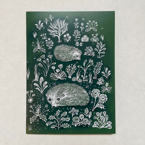 Dark green greetings card with white illustrations of two hedgehogs walking amongst the flowers and plants 