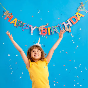 here the bunting is seen behind a young child jumping for joy.  The letters of the bunting are brightly coloured in red, yello, green, blue and pink.  Various animals can be seen along the length including a zebra, giraffe, sloth, crocodile and monkey.  All the aniamals are wearing party hats.