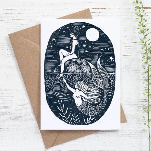 Blank inside.  Gretings card featuring a woman in swimming costume sitting on a rock under the stars.  beneath her a mermaid is swimming and reaching out to touch her submerged foot.  Design taken from a linocut by Nicole Revy of Prints by The Bay, Dorset, UK