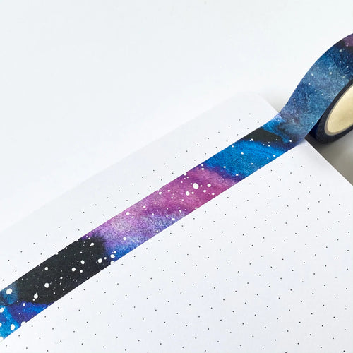 this photo shows the washi tape stuck accross a page showing the colours from black, purples and blues making up the backgpround of the galaxy with little white dots (planets and stars) dotted over.