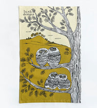 Load image into Gallery viewer, this tea towel is printed in green and black and white.  It features 4 baby owls sitting in pairs in 2 branches of a tree.  A green hill with trees on top can be seen on the background.
